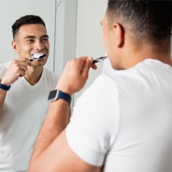 man brushing teeth in bathroom mirror 
