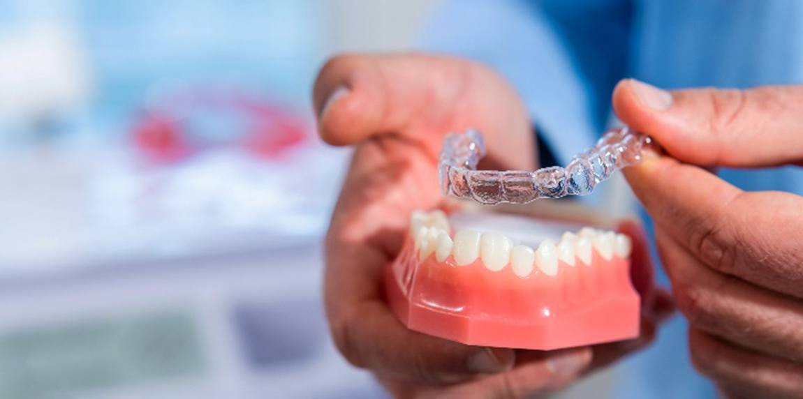 Dentist placing Invisalign aligner over model of teeth