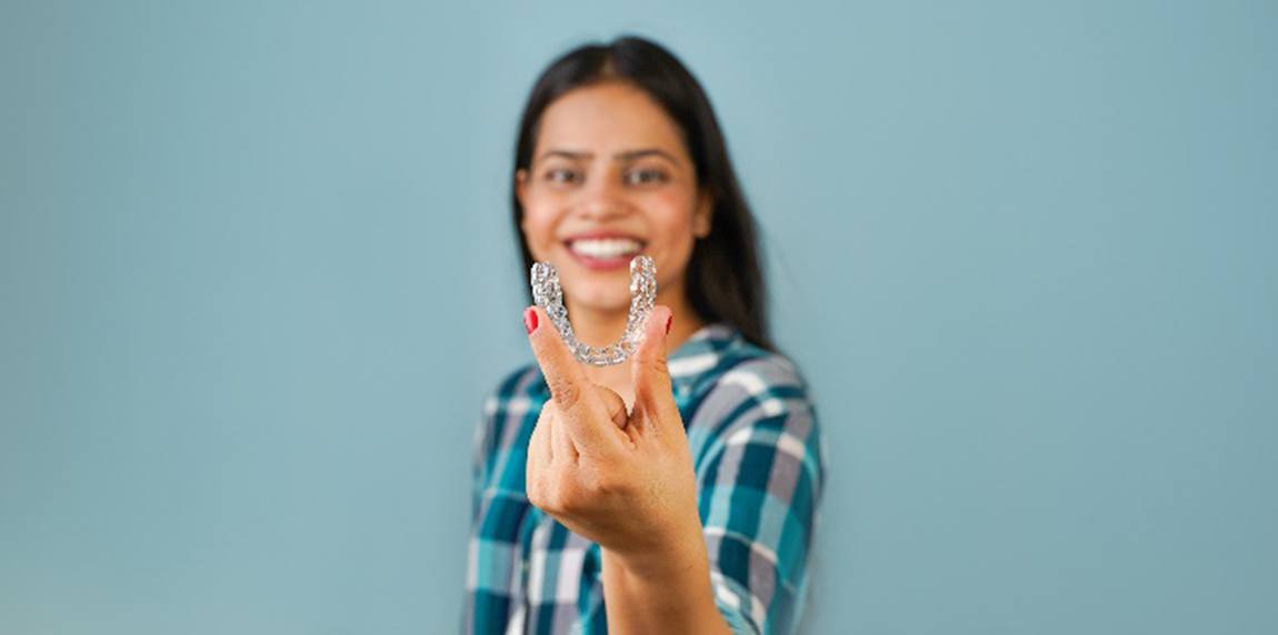 Woman in plaid shirt smiling while holding clear aligner